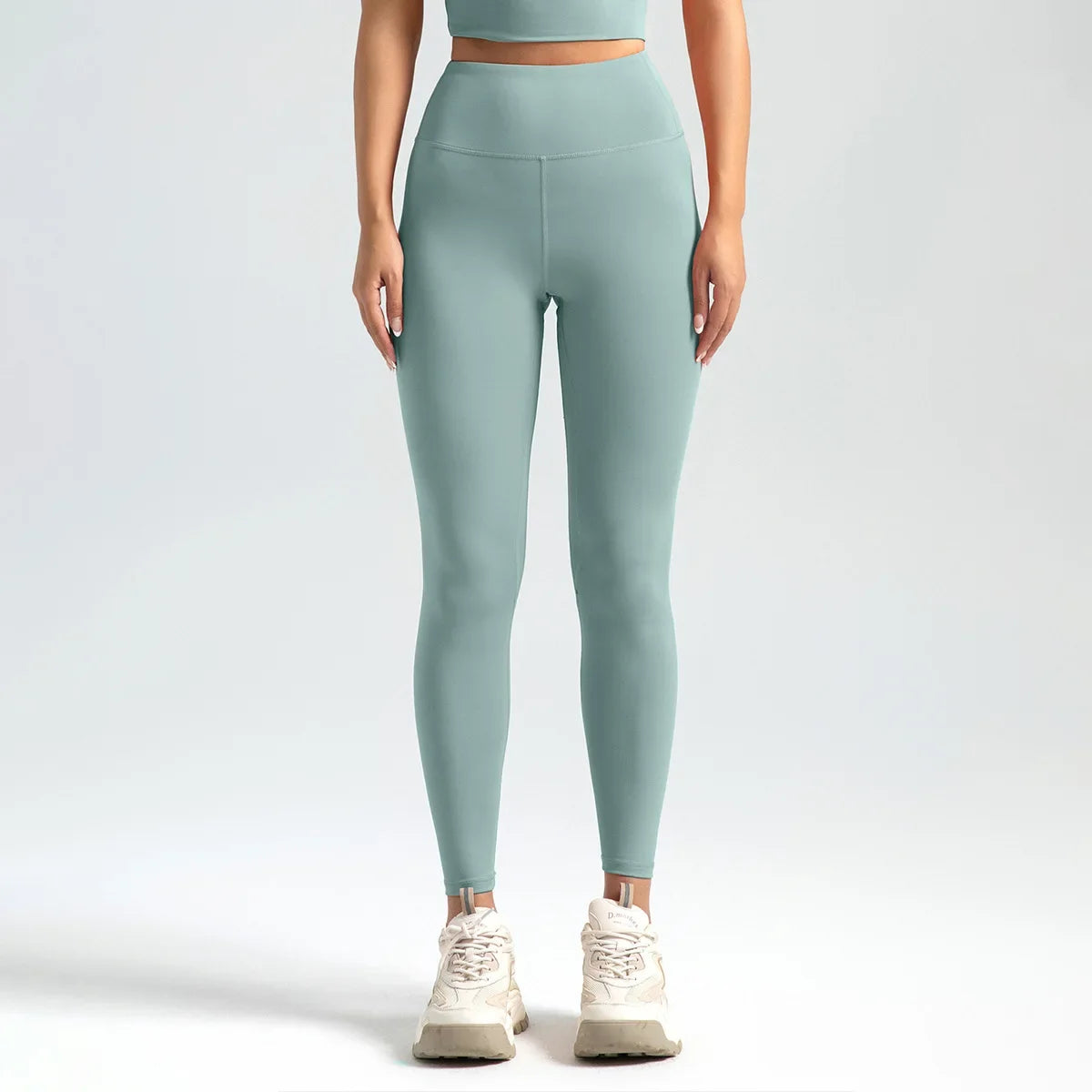 A woman wearing high-waist seamless booty-lifting yoga leggings in dark green color, paired with a sports bra and white sneakers.