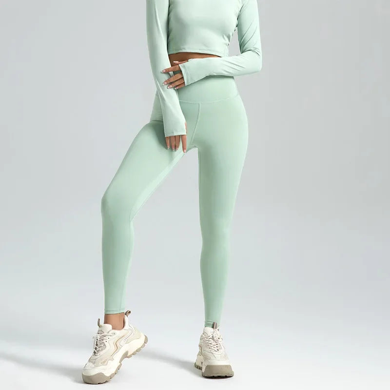 A woman wearing high-waist seamless booty-lifting yoga leggings in light green color, paired with a sports bra and white sneakers.
