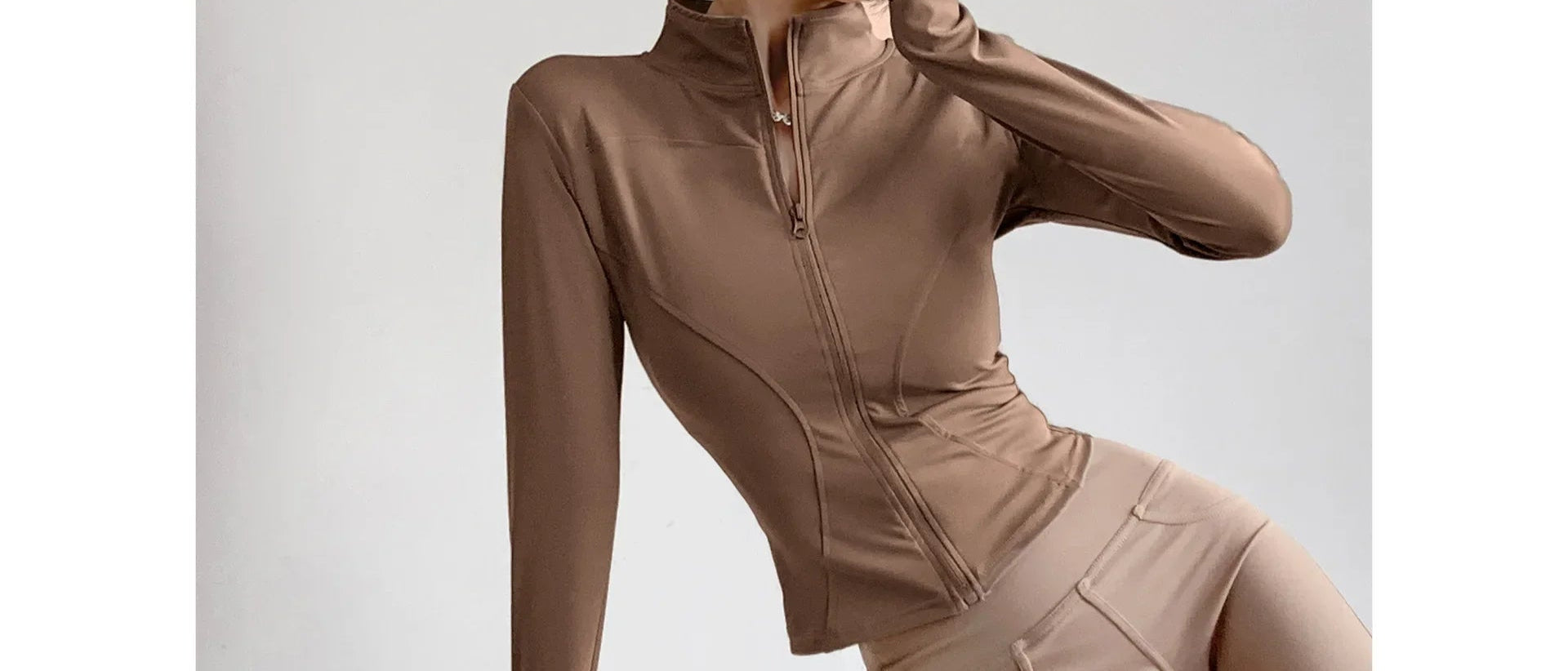 Beige long-sleeve athletic top with a high collar on a light gray background