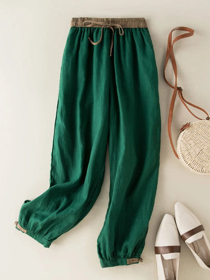 Green pants with a drawstring on a light background, accompanied by a woven bag and white shoes.