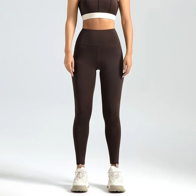 A woman wearing high-waist seamless booty-lifting yoga leggings in dark coffee color, paired with a sports bra and white sneakers.