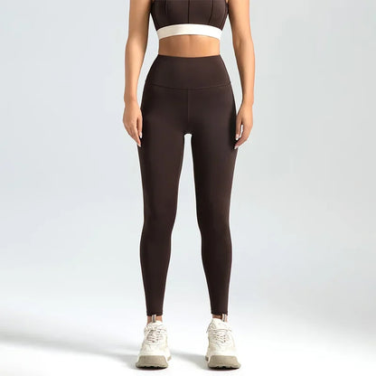 A woman wearing high-waist seamless booty-lifting yoga leggings in dark coffee color, paired with a sports bra and white sneakers.