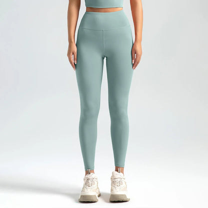 A woman wearing high-waist seamless booty-lifting yoga leggings in dark green color, paired with a sports bra and white sneakers.