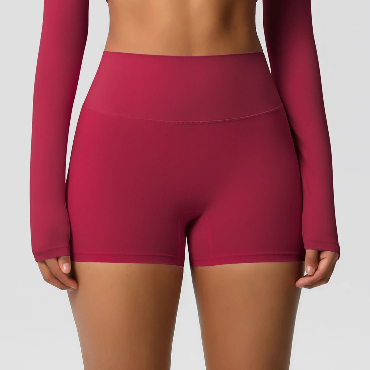 A pair of high-waist red yoga shorts, worn with a matching long-sleeve top and white sneakers, suitable for fitness support during workouts or daily activities.