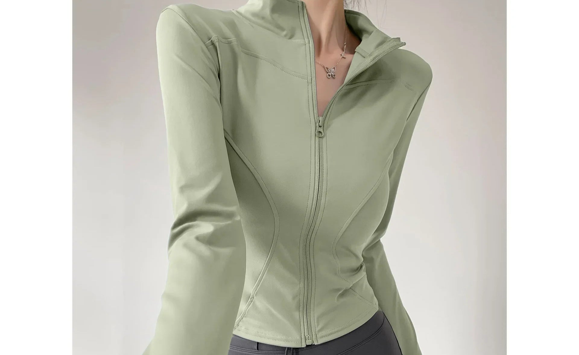 Person wearing a green jacket and gray leggings on a plain background