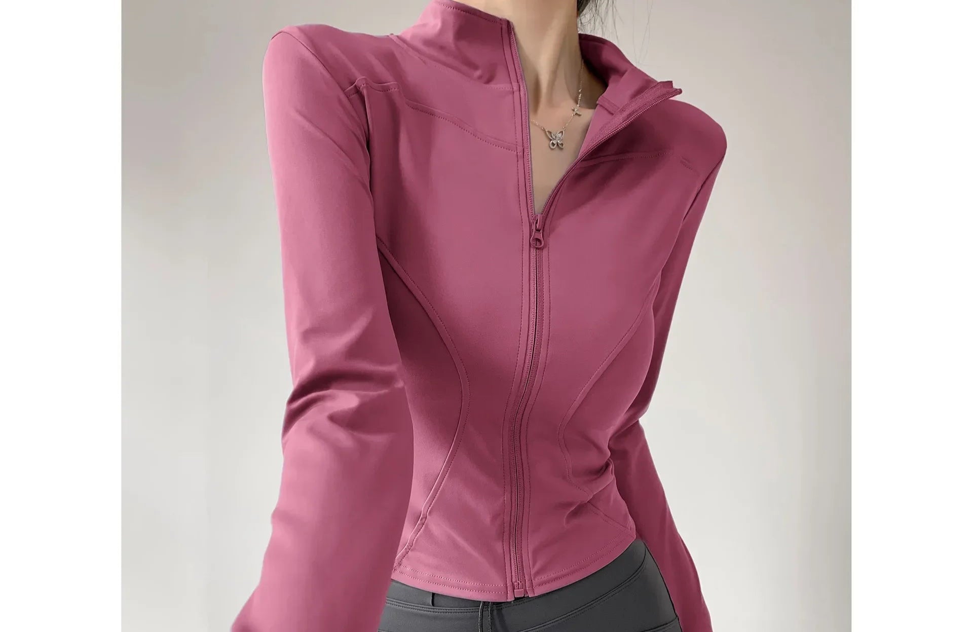 Person wearing a pink jacket and gray pants on a plain background