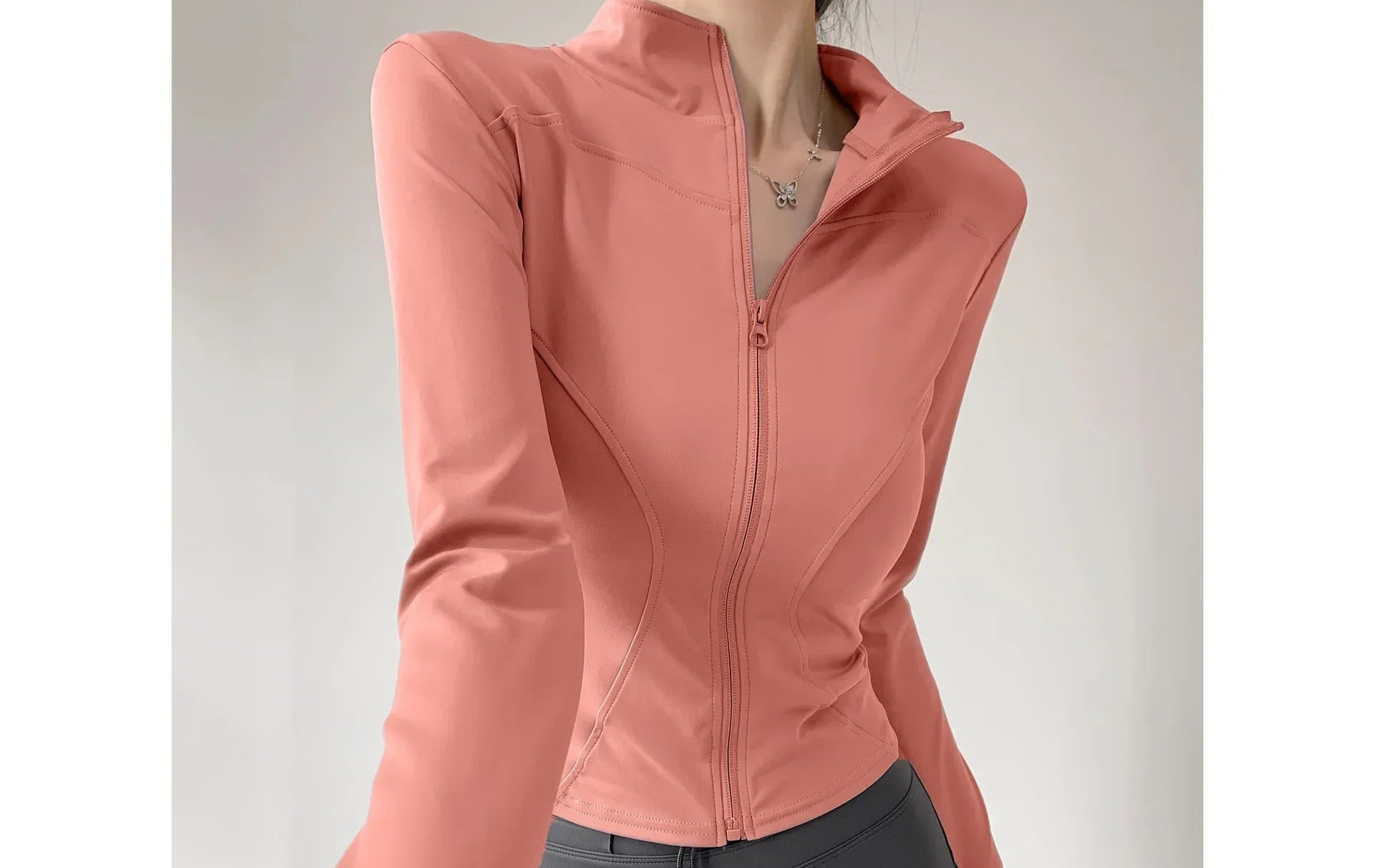 Person wearing a pink zip-up jacket and gray leggings on a plain background