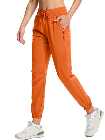 A pair of orange athletic pants with an elastic waistband and drawstring, featuring side pockets and a full-length design.
