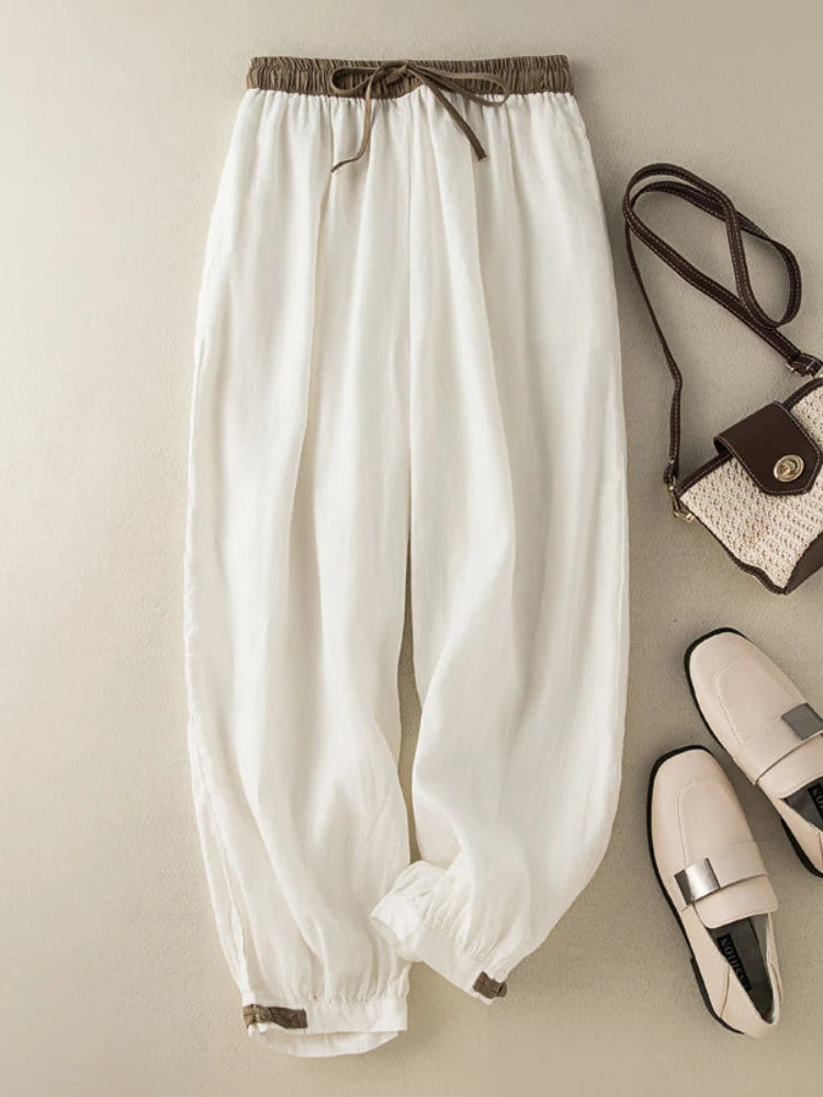 White pants with brown drawstring, a small handbag, and white shoes on a beige background
