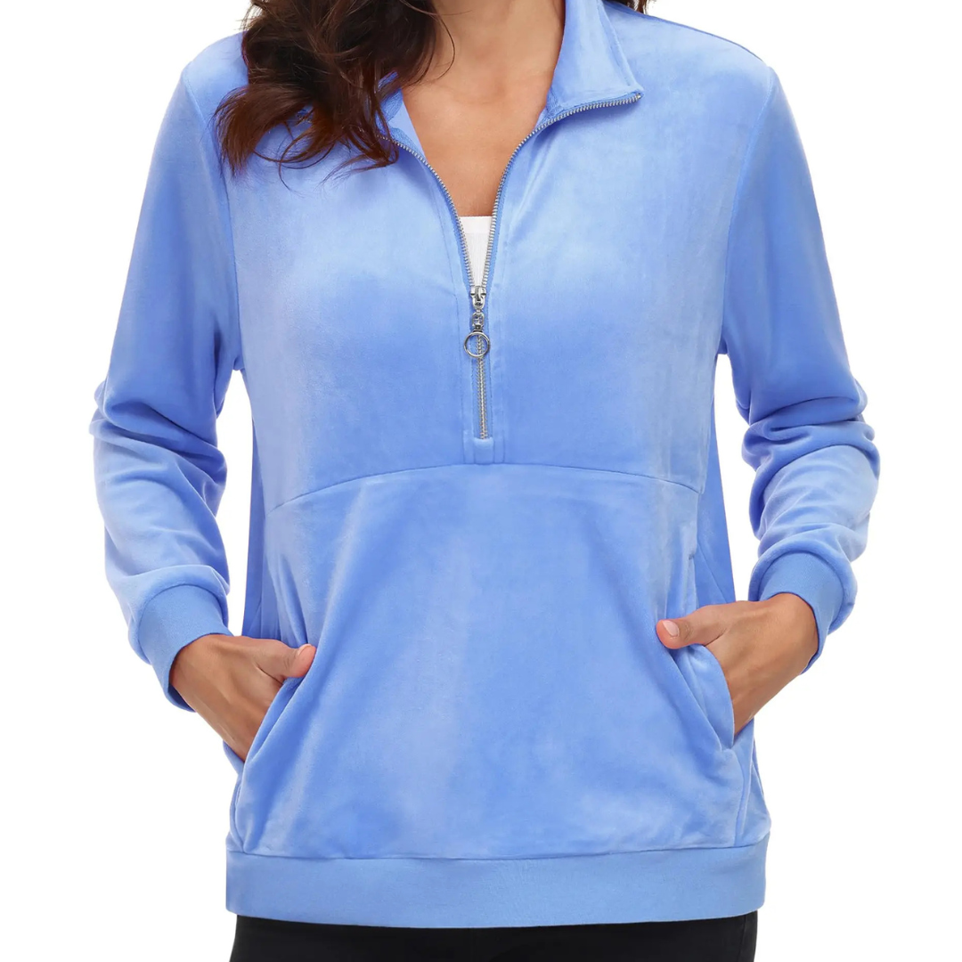 A woman wearing a light blue half zip fleece pullover hoodie with a hood, standing with hands in pockets.