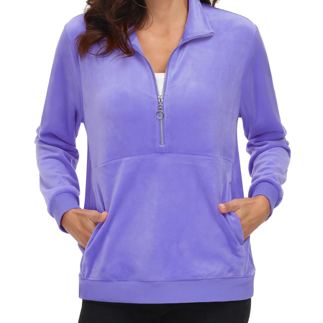 A woman wearing a light purple half zip fleece pullover hoodie with a hood, standing with hands in pockets.