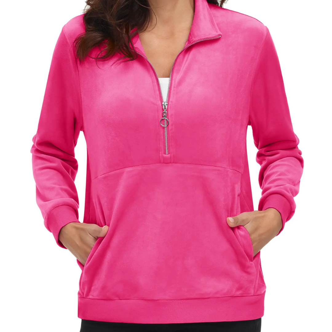 A woman wearing a phosphor pink half zip fleece pullover hoodie with a hood, standing with hands in pockets.