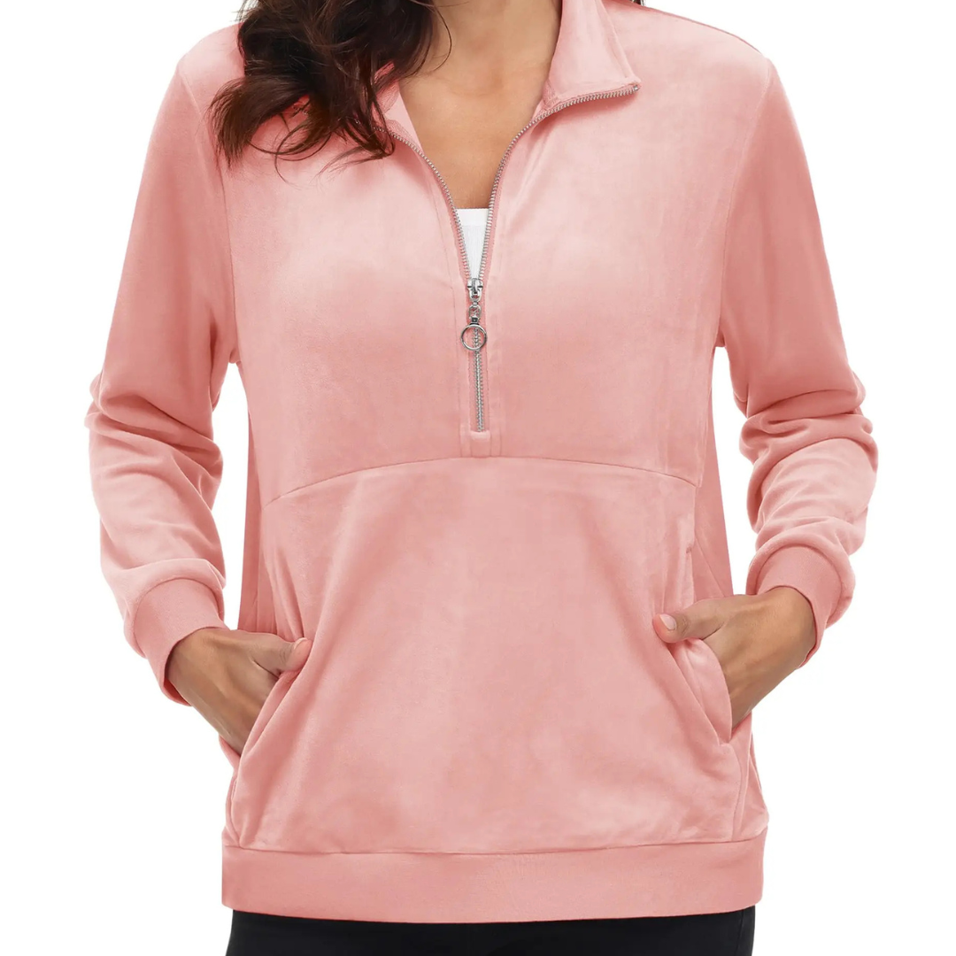 A woman wearing a pink half zip fleece pullover hoodie with a hood, standing with hands in pockets.