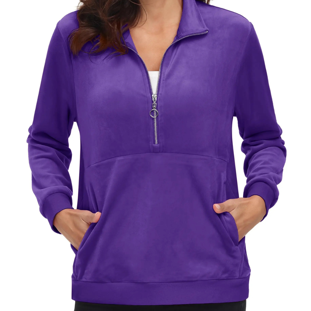A woman wearing a purple half zip fleece pullover hoodie with a hood, standing with hands in pockets.