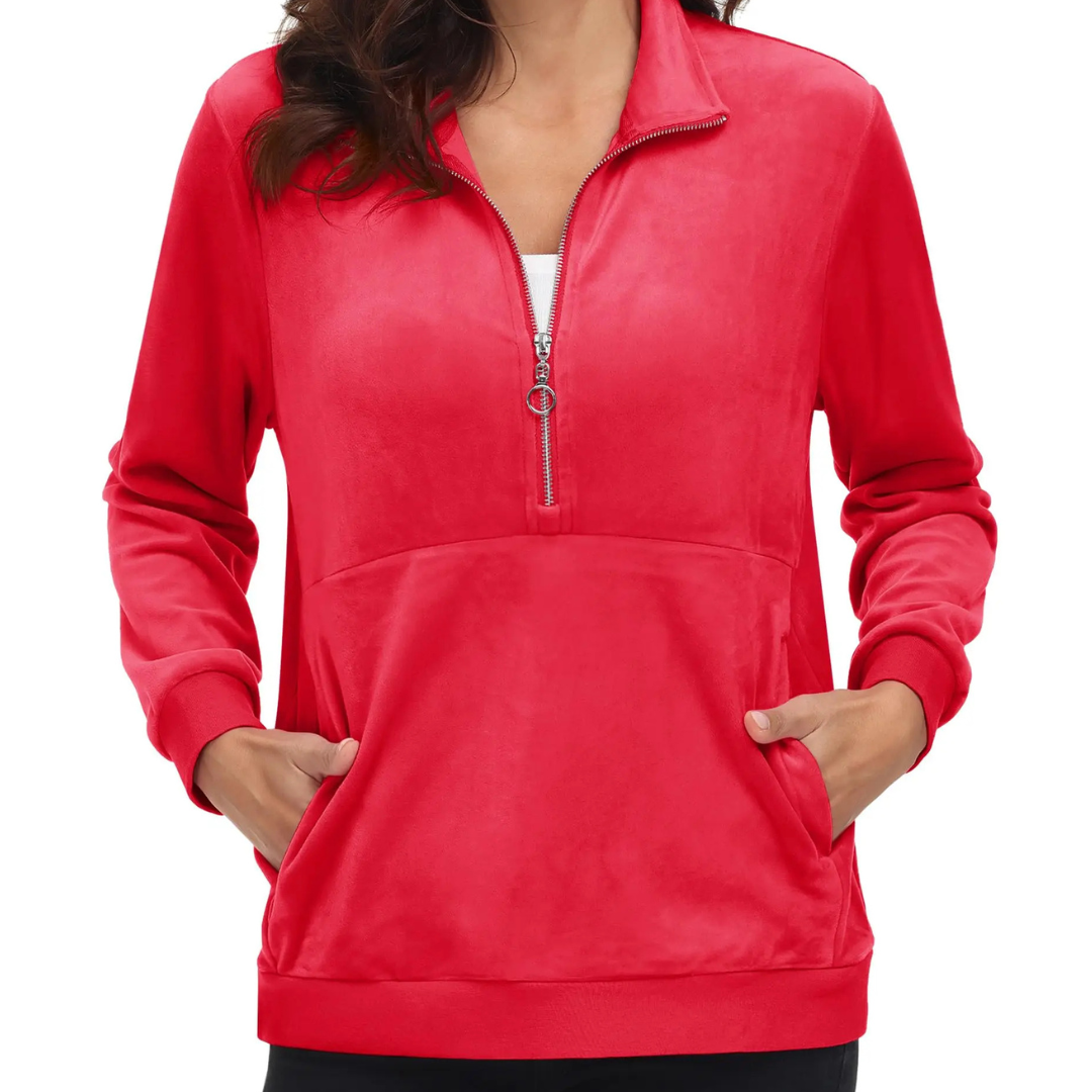 A woman wearing a tomato red half zip fleece pullover hoodie with a hood, standing with hands in pockets.