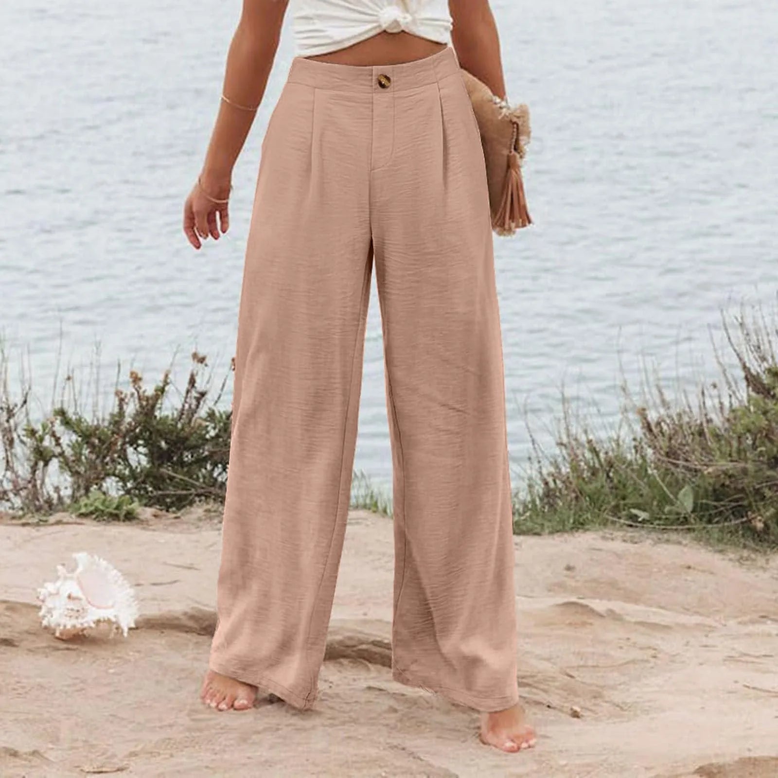 Person wearing beige wide-leg pants standing on a beach with a blurred background