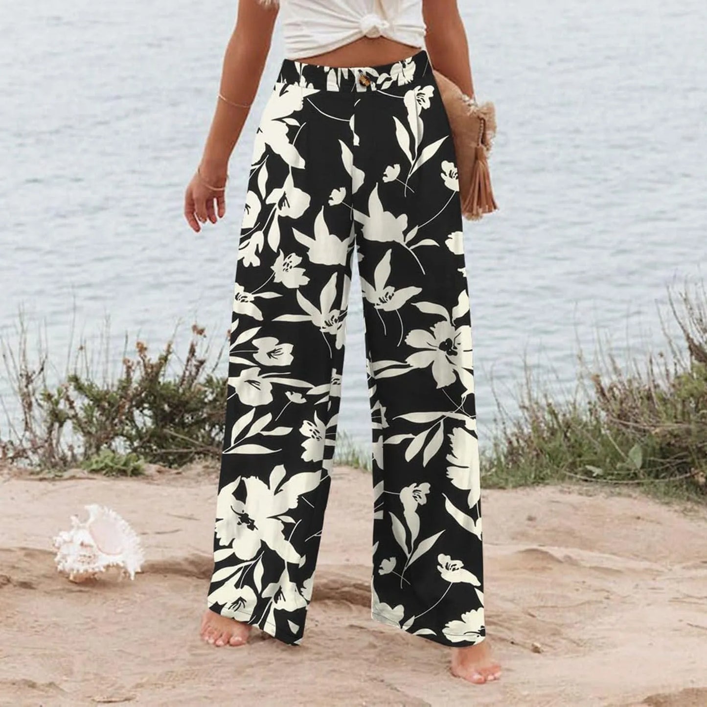 Person wearing black floral pants standing on a beach.
