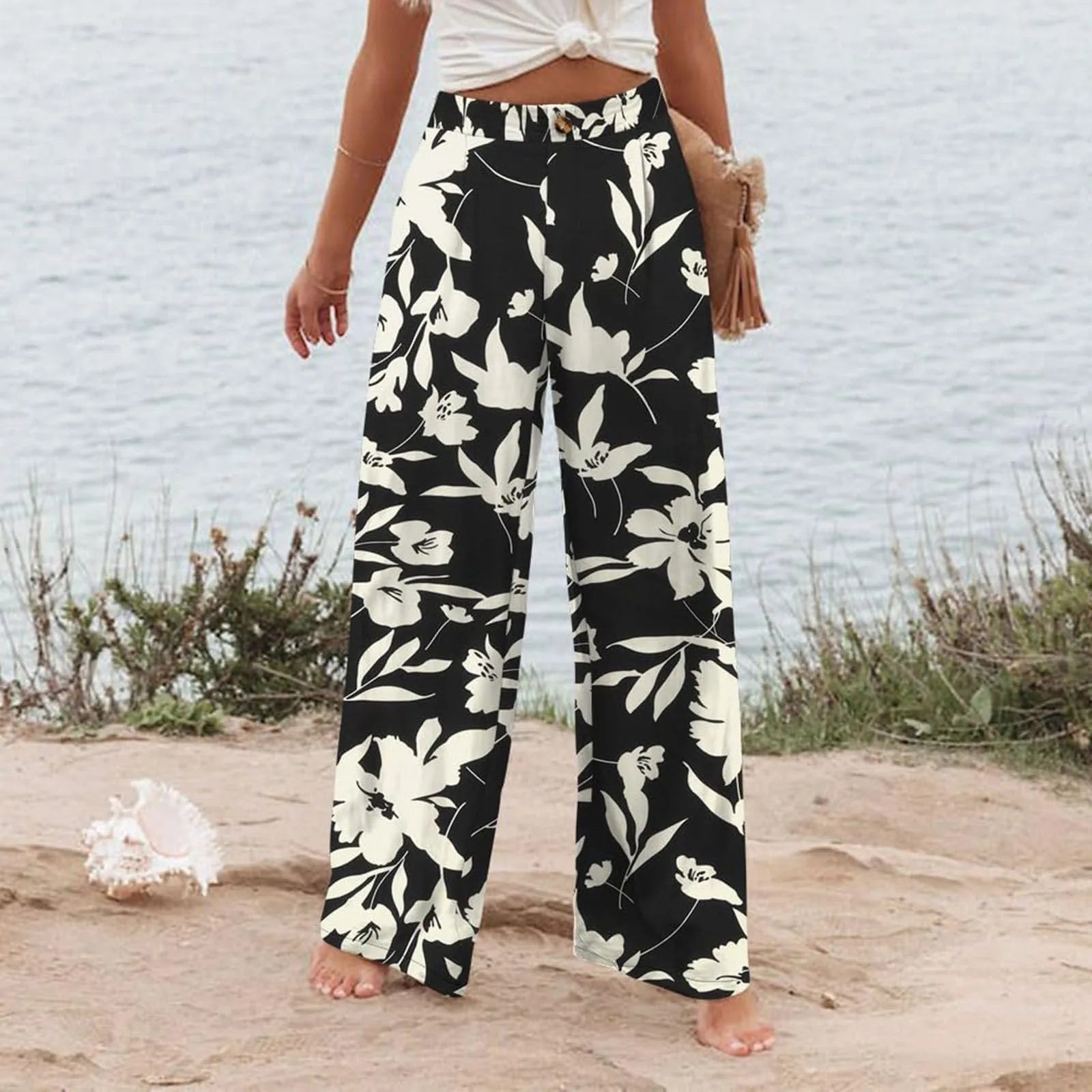 Person wearing black floral pants standing on a beach.